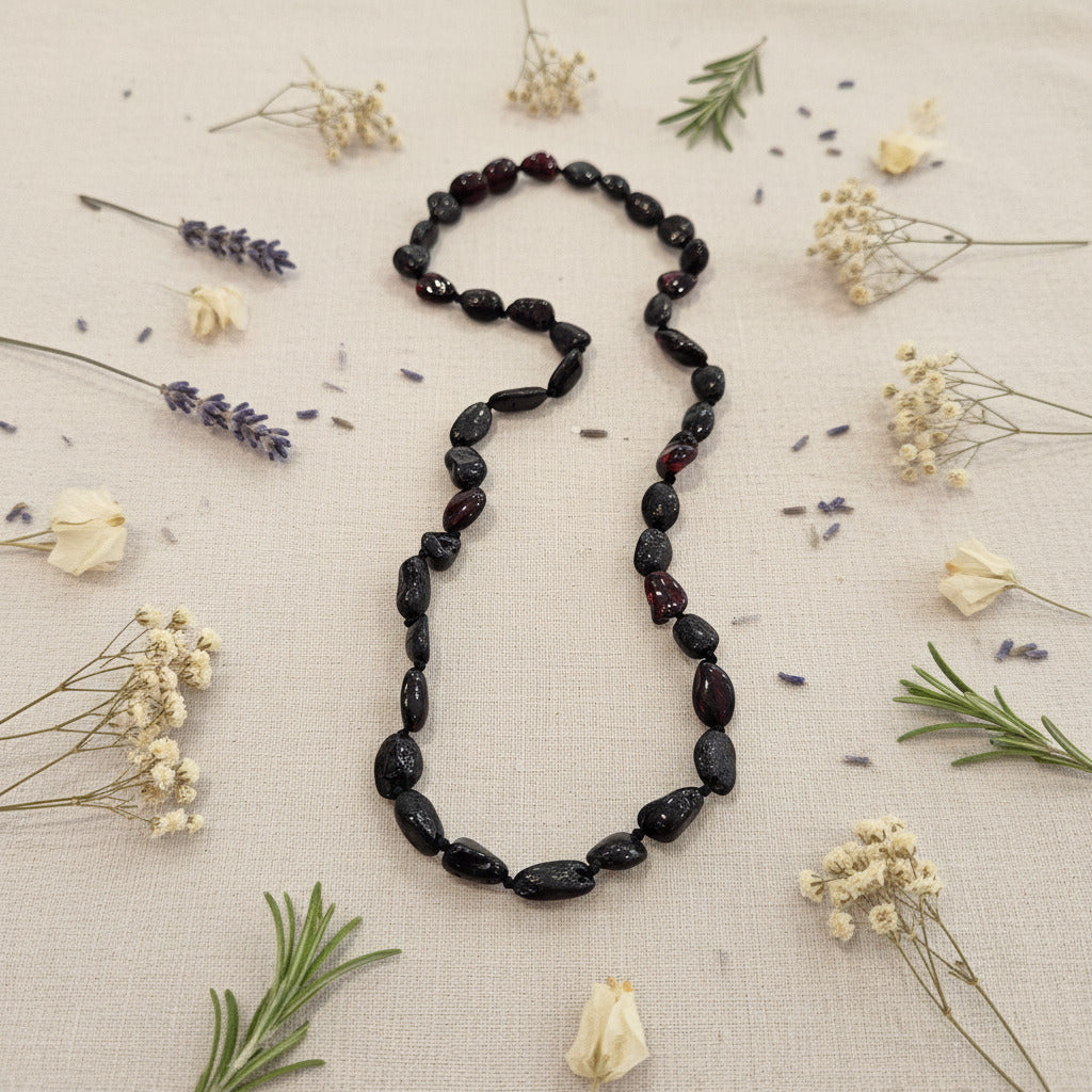 Black Amber Necklace on a light fabric background with dried flowers