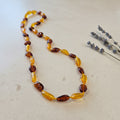 Necklace with amber beads on a light surface with lavender flowers.
