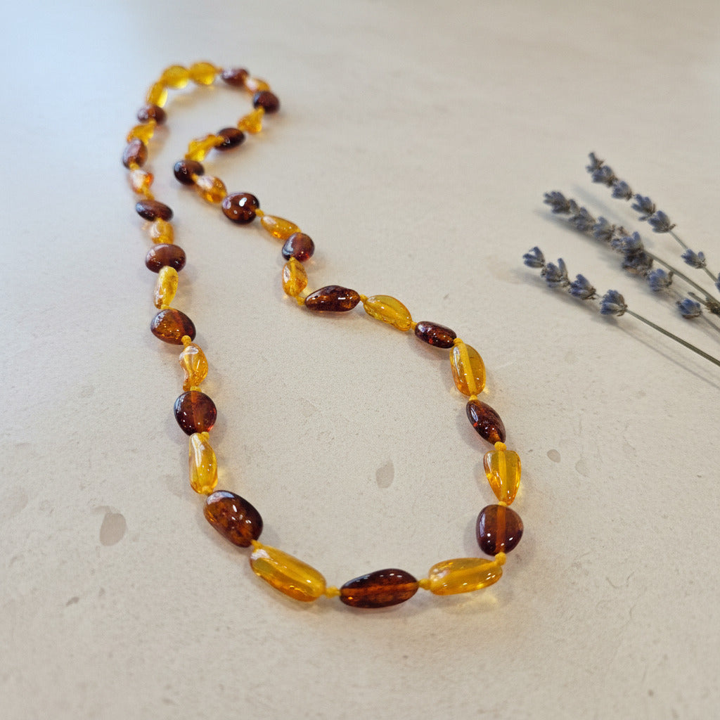 Necklace with amber beads on a light surface with lavender flowers.