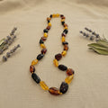 Amber Necklace with multicolored beads on a beige fabric background with lavender and green leaves.