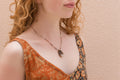 Woman wearing a patterned top and a dainty necklace against a beige background