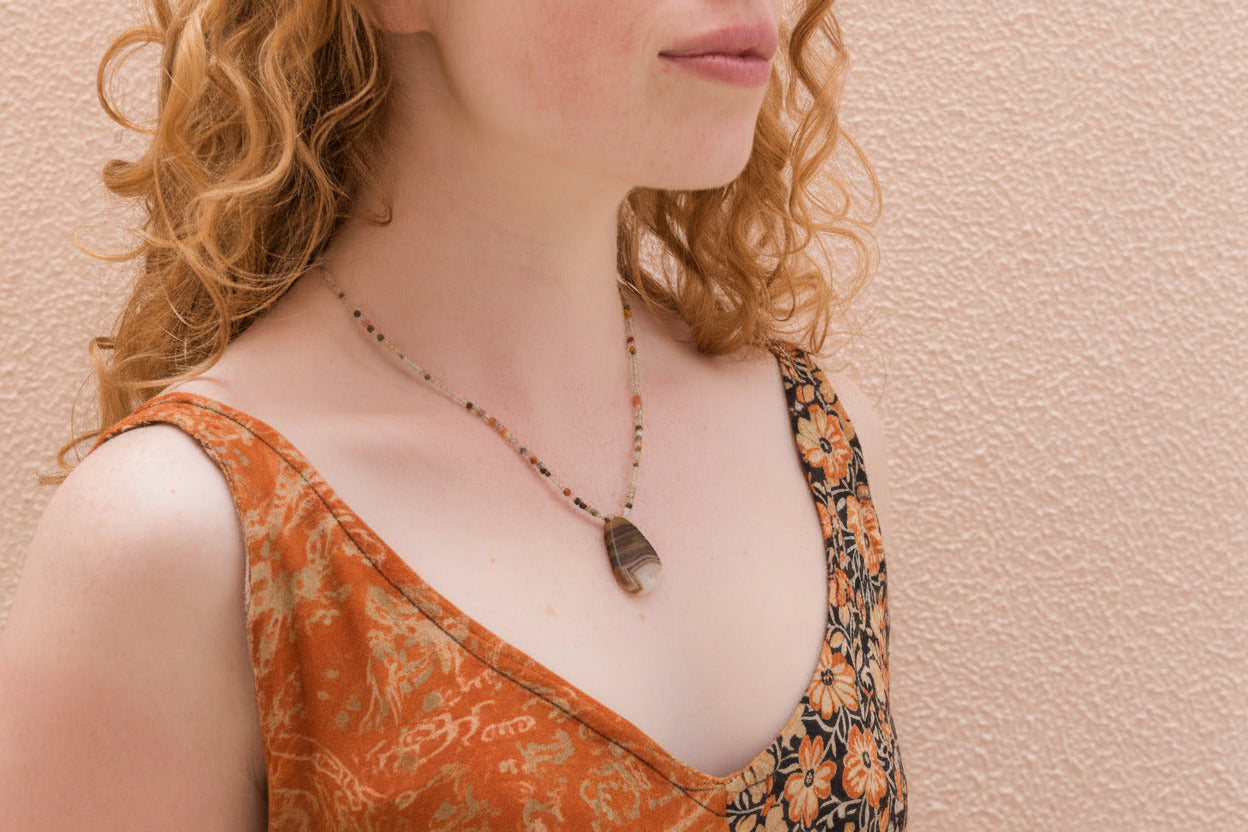 Woman wearing a patterned top and a dainty necklace against a beige background