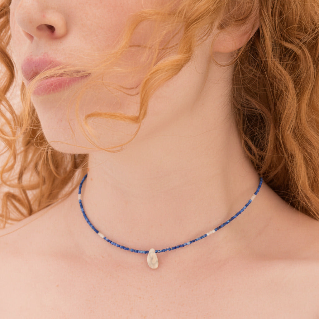 Close-up of a woman wearing a blue beaded necklace with a stone pendant.