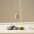 Necklace with a pendant featuring a floral design, placed on a neutral background with stones and a small plant.