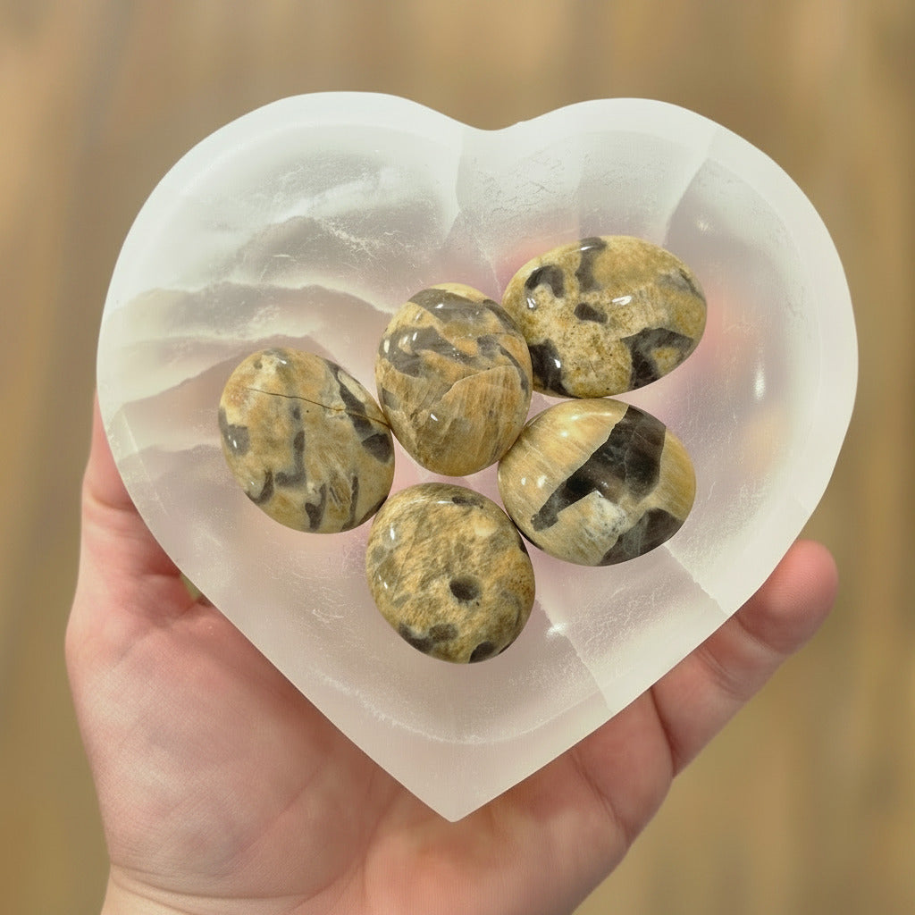 Heart-shaped crystal with marbled stones held in a hand against a blurred background