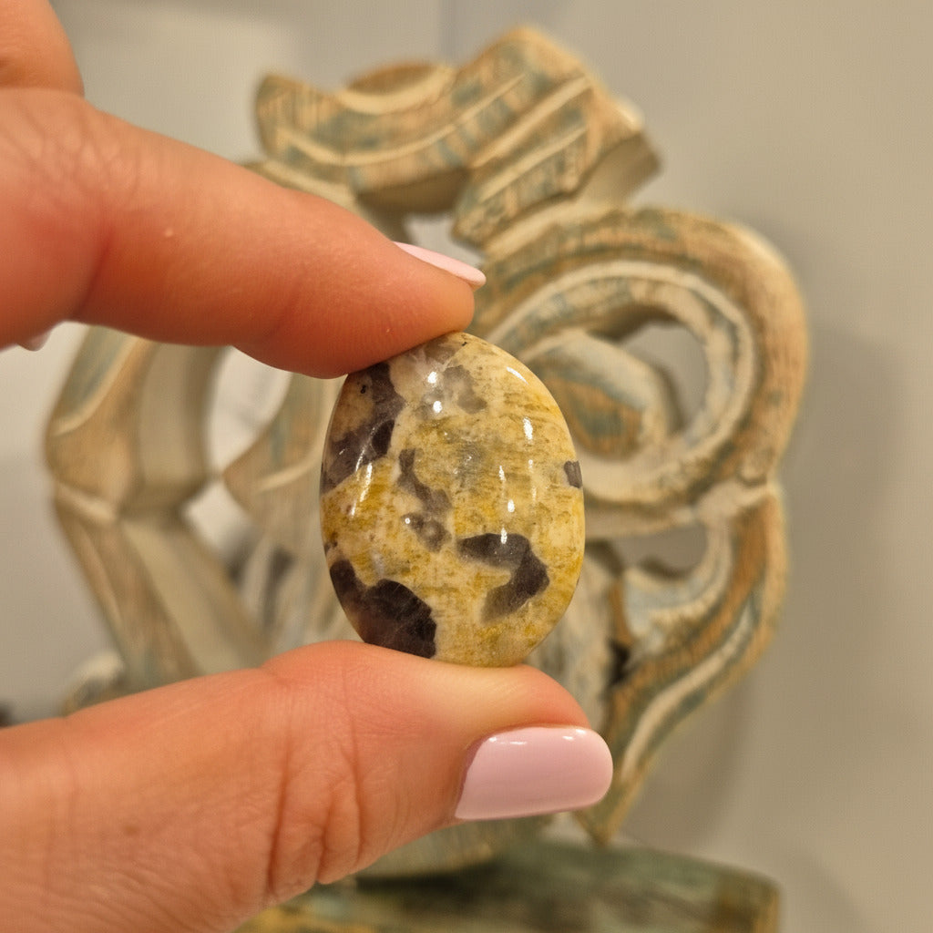 Hand holding a patterned stone with a decorative object in the background