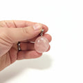 Pink crystal pendant held between fingers with a white background