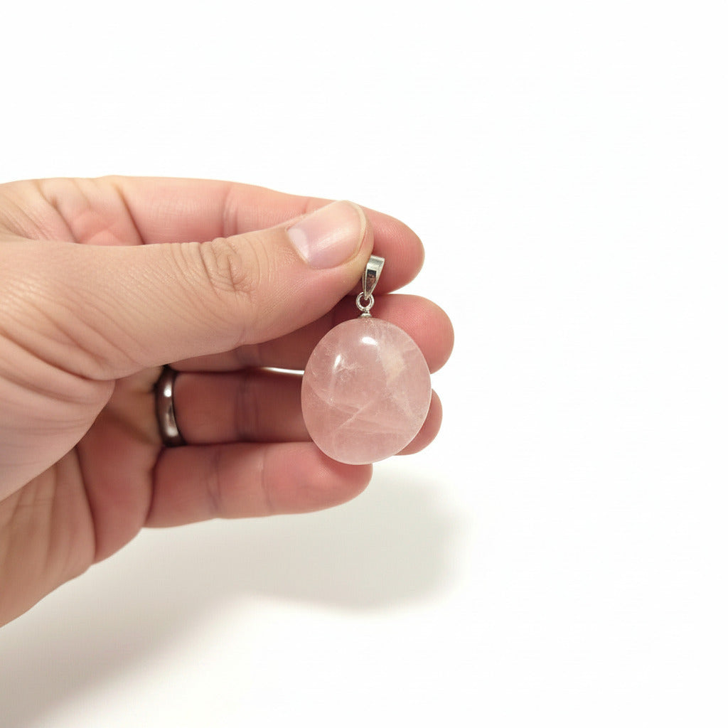 Pink crystal pendant held between fingers with a white background