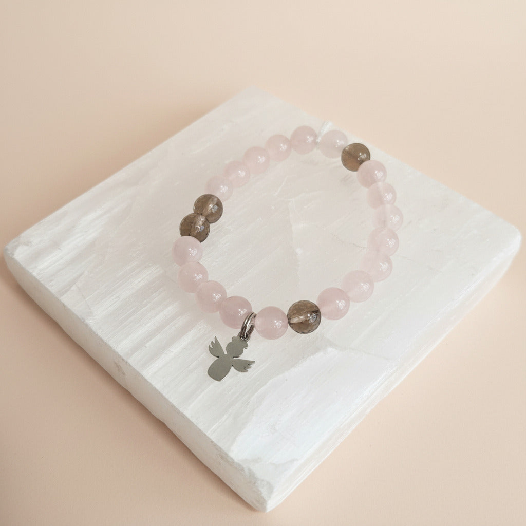 Pink beaded bracelet with a silver charm on a white tray with a beige background