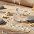 Silver necklace with a clear pendant on a sandy surface