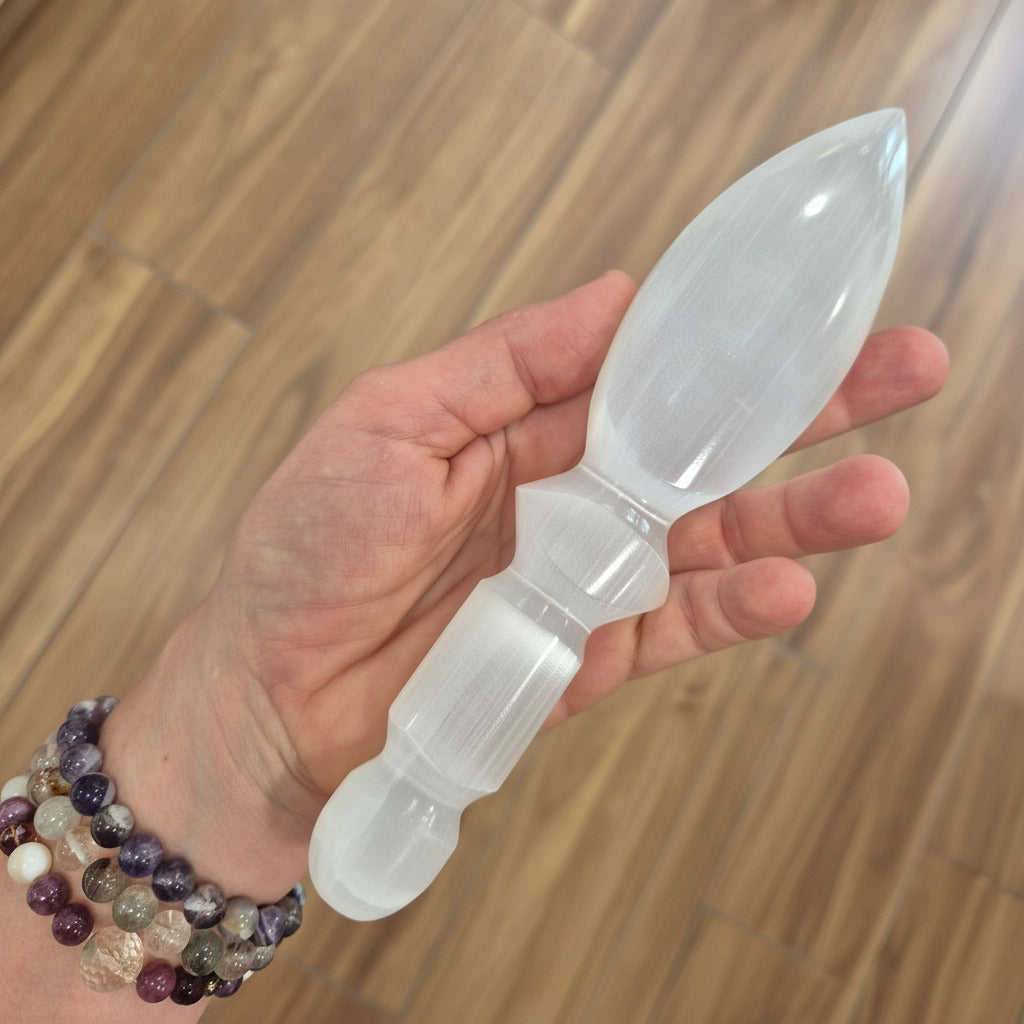 Selenite sward held in a hand with a wooden floor background