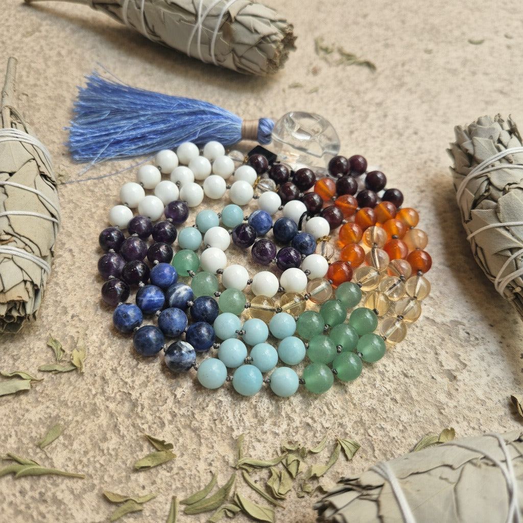 Colorful beaded neklace on a textured surface with smudge sticks and herbs.