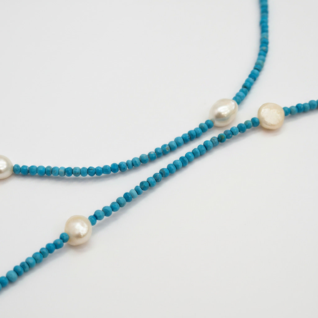 A beaded necklace with small turquoise-blue beads and three large white pearl-like accents, laid on a white background.