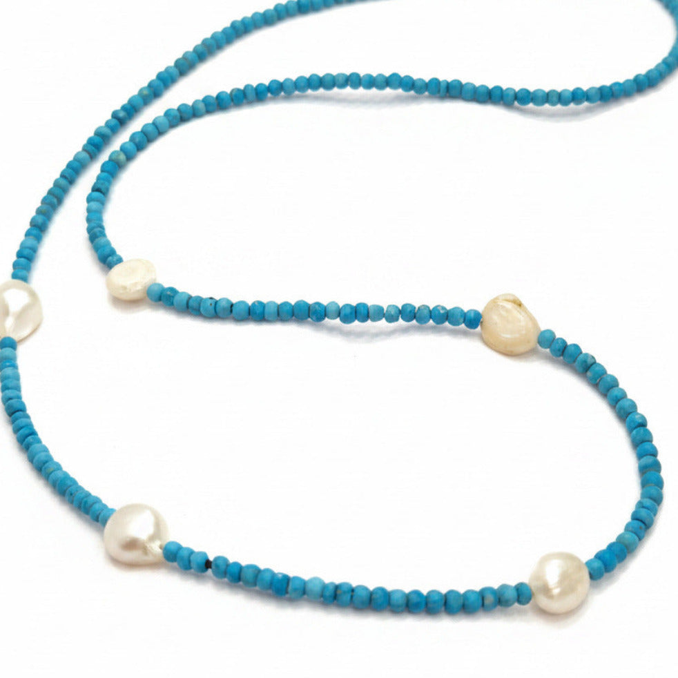 A beaded necklace featuring small, faceted turquoise-blue beads with irregular, cream-colored baroque pearls spaced along the strand, displayed on a clean white background.