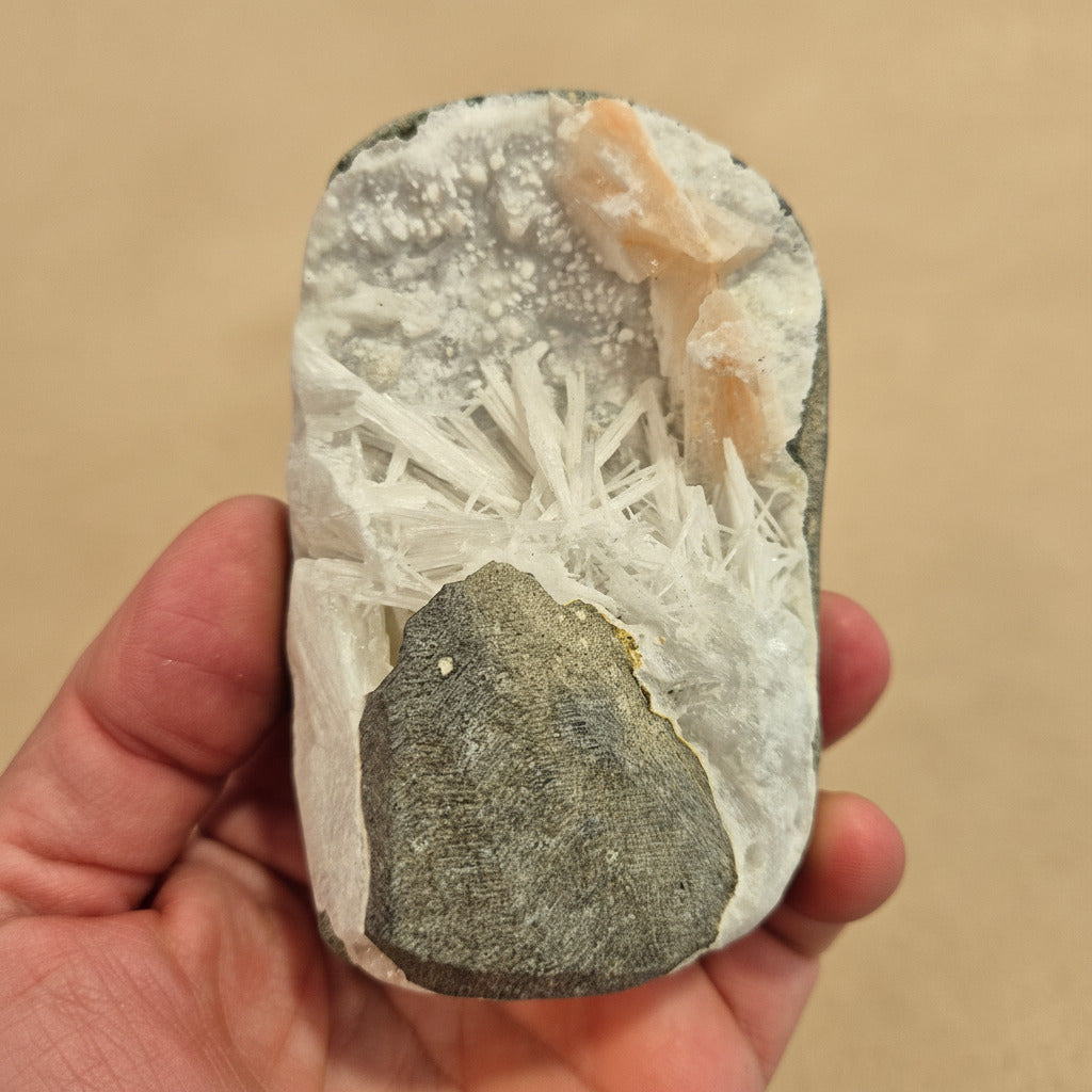 Hand holding a rock with crystals against a beige background