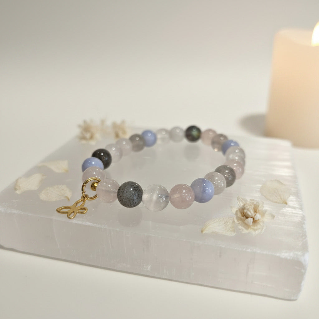 Pastel gemstone bracelet with gold butterfly charm on selenite slab, calming zen aesthetic
