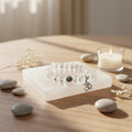 Bracelet with a silver charm on a white stand, surrounded by stones and a candle on a wooden surface.