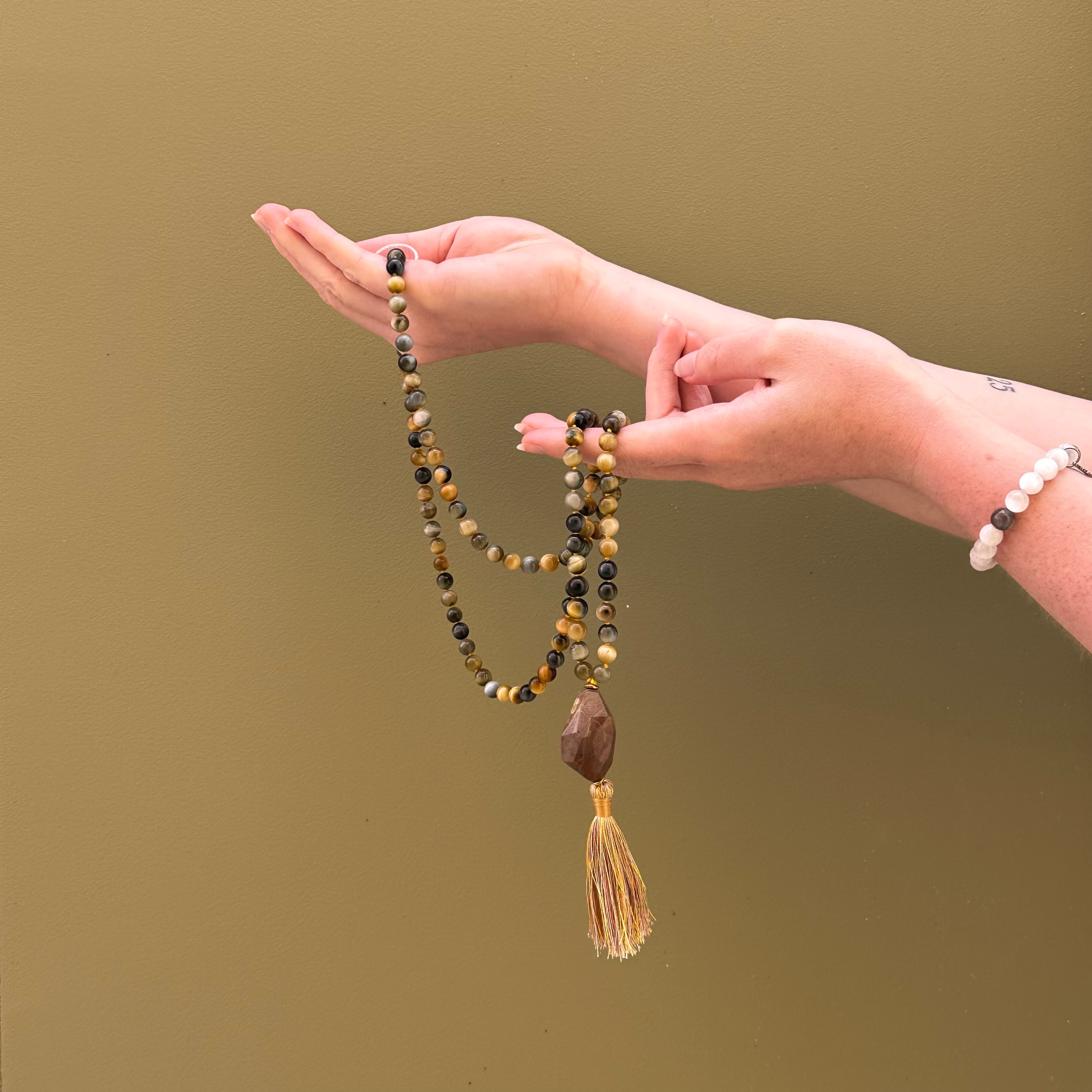 Hand holding a beaded necklace with a tassel against a plain background