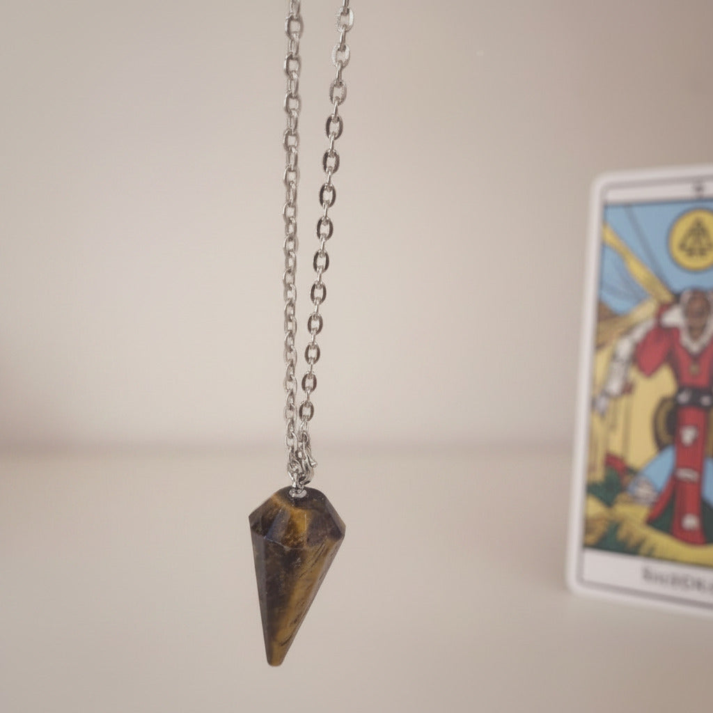 Tiger eye pendulum on a chain with a blurred tarot card in the background
