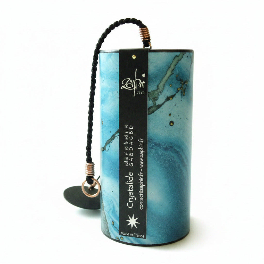 A cylindrical Zaphir chime in a blue and teal marbled colored, featuring a black hanging cord with brass-colored end caps and a black paper label with white text.