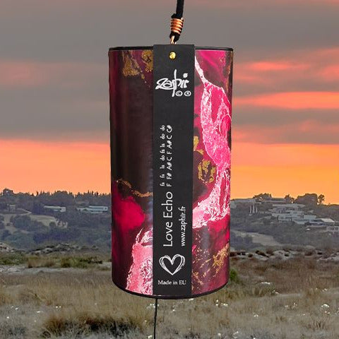 A rectangular Zaphir chime labeled 'Love Echo' is shown against a sunset landscape with a train track and grassy field. The package has a black background with pink floral graphics and white text.