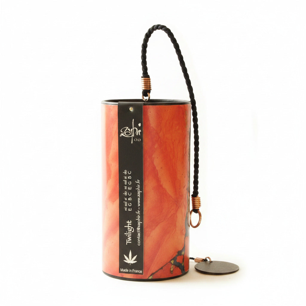 A cylindrical zaphir chime with a marbled red and orange pattern, featuring a black side label with white text and a black braided hanging cord with metal rings.