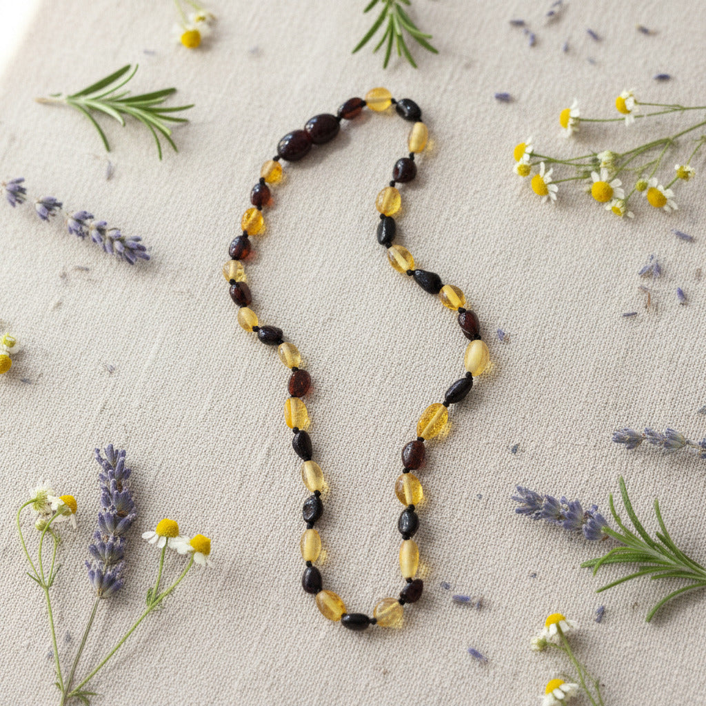 A beaded necklace made of alternating translucent amber-yellow and dark brown polished beads, laid out on a rustic beige surface with dried flowers and herbs