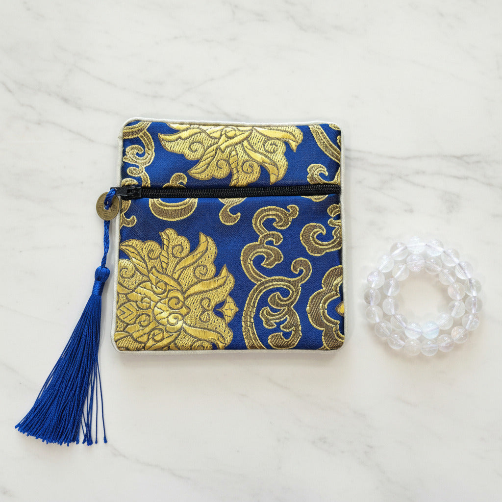 Blue and gold patterned pouch with tassel on a white surface