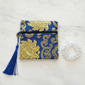 Blue and gold patterned pouch with tassel on a white surface