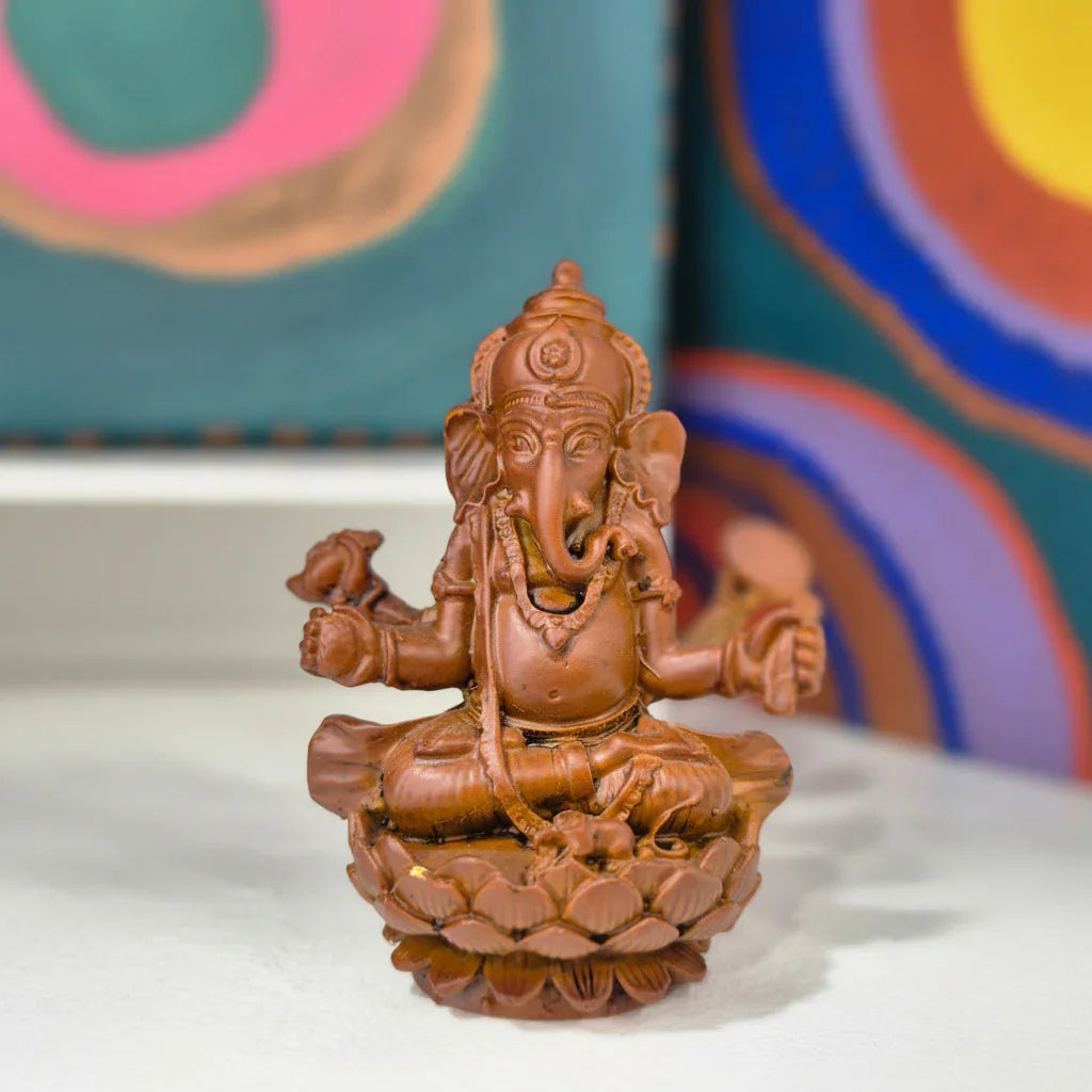 Brown statue of a seated figure on a white surface with colorful abstract art in the background
