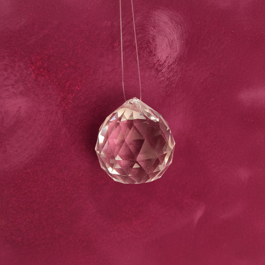 A faceted clear crystal  with a pink tint, threaded on a clear string, set against a textured dusty pink background.