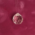 A faceted clear crystal  with a pink tint, threaded on a clear string, set against a textured dusty pink background.