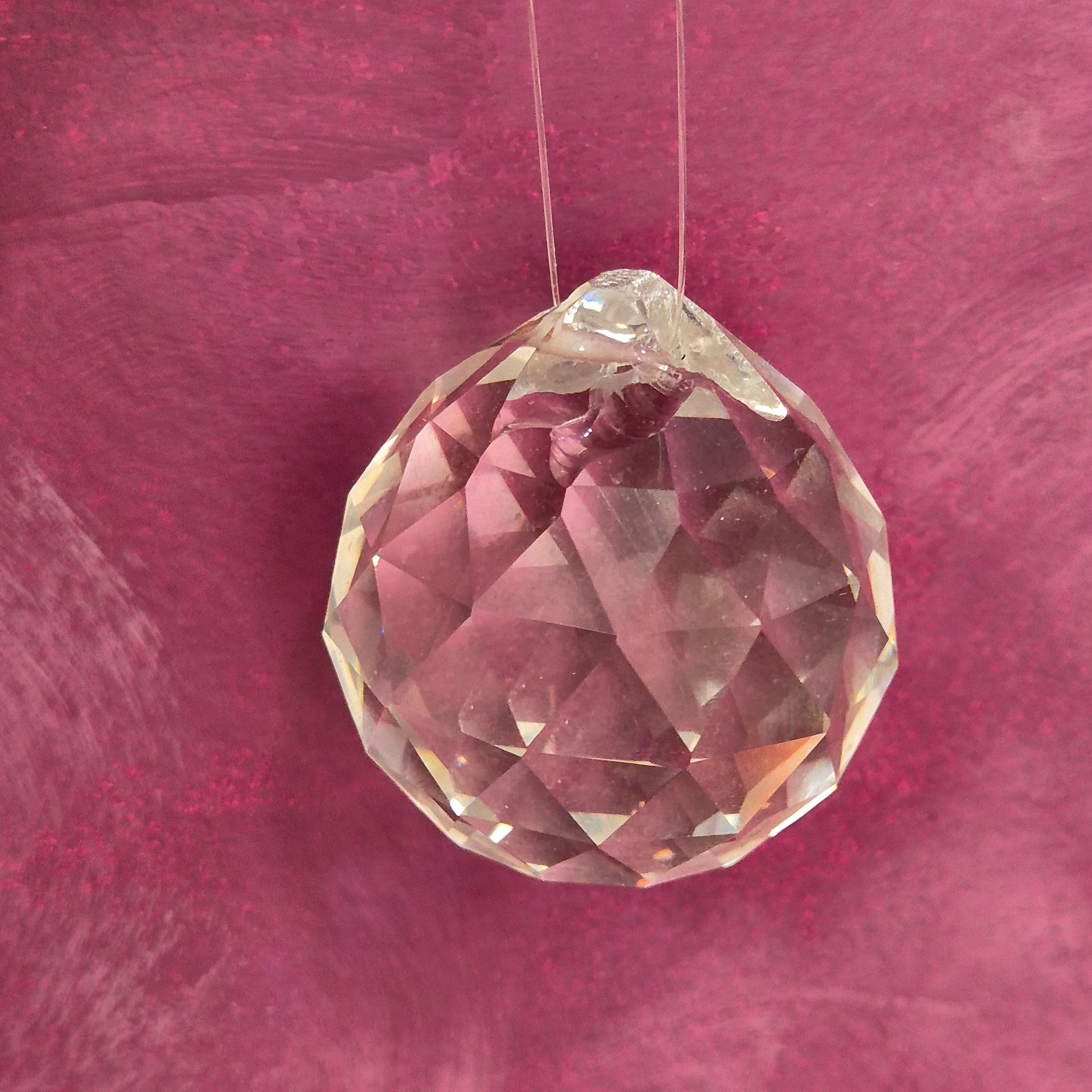 A faceted glass bead threaded on a clear string, set against a textured magenta-pink background.