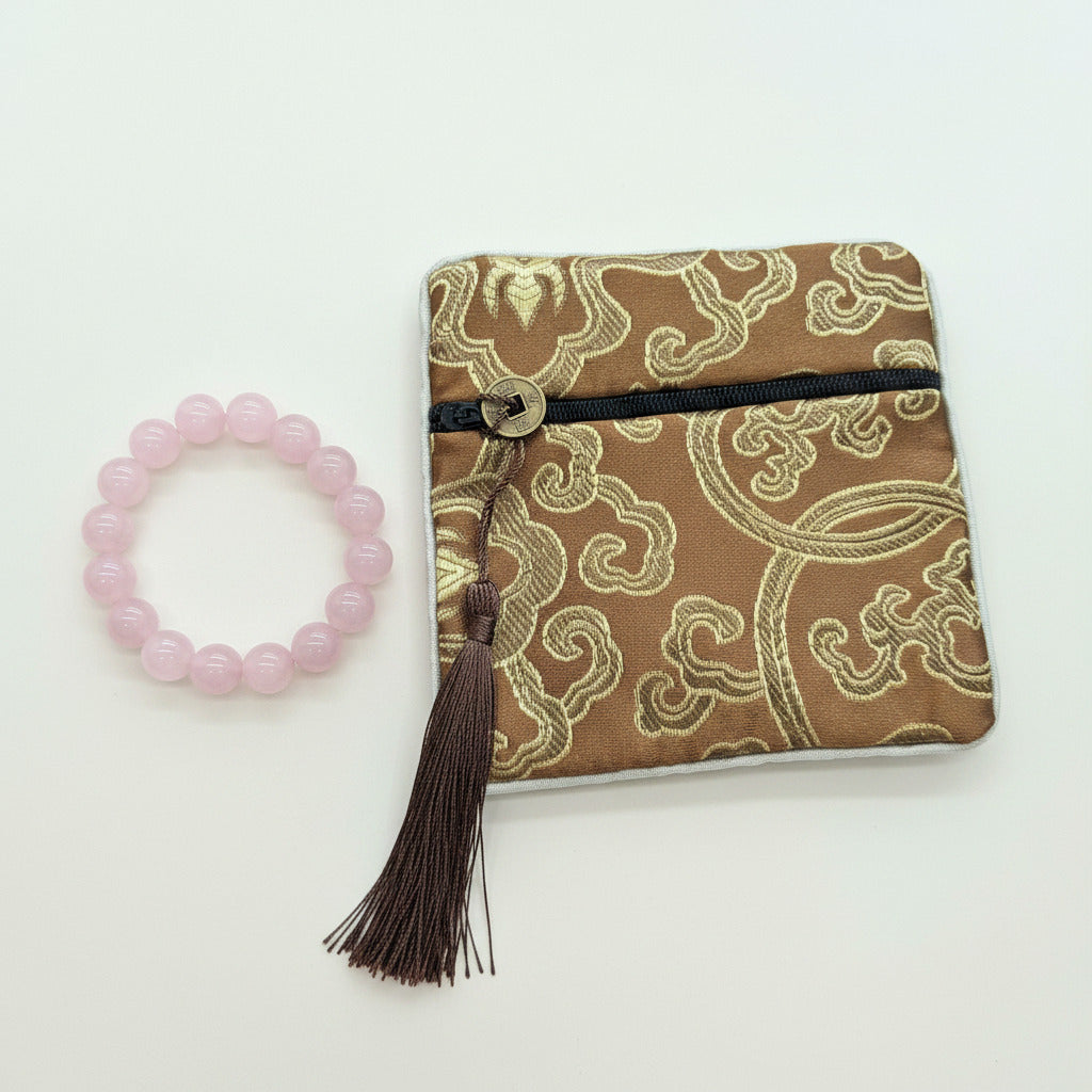 Decorative pouch with tassel and pink beaded bracelet on a white background