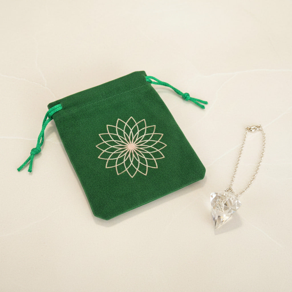 Green velvet pouch with gold lotus design beside clear crystal pendant necklace