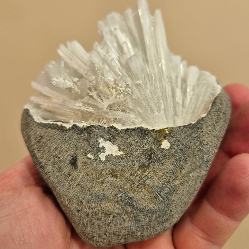 Hand holding a rock with crystal formations against a beige background