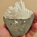 Hand holding a rock with crystal formations against a beige background
