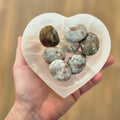 Heart-shaped white stone with green and brown marbled stones on a blurred beige background