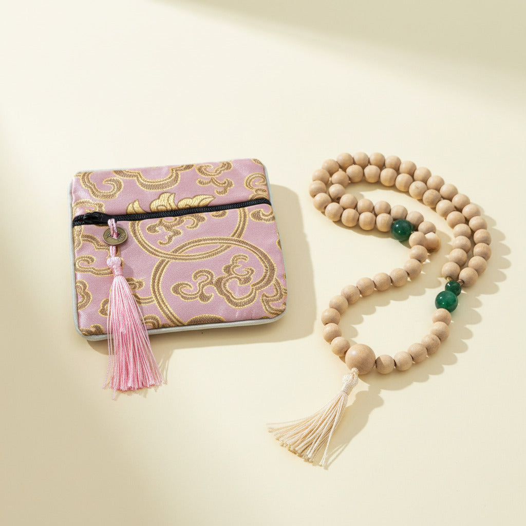 Pink and gold patterned pouch with tassel next to a wooden beaded necklace on a beige background