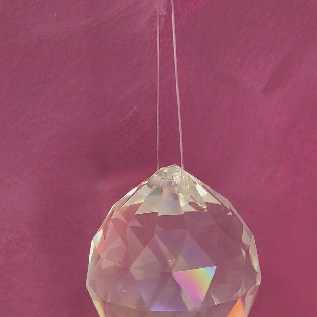 Faceted crystal feng shui is hanging and spinning around in a magenta bacground
