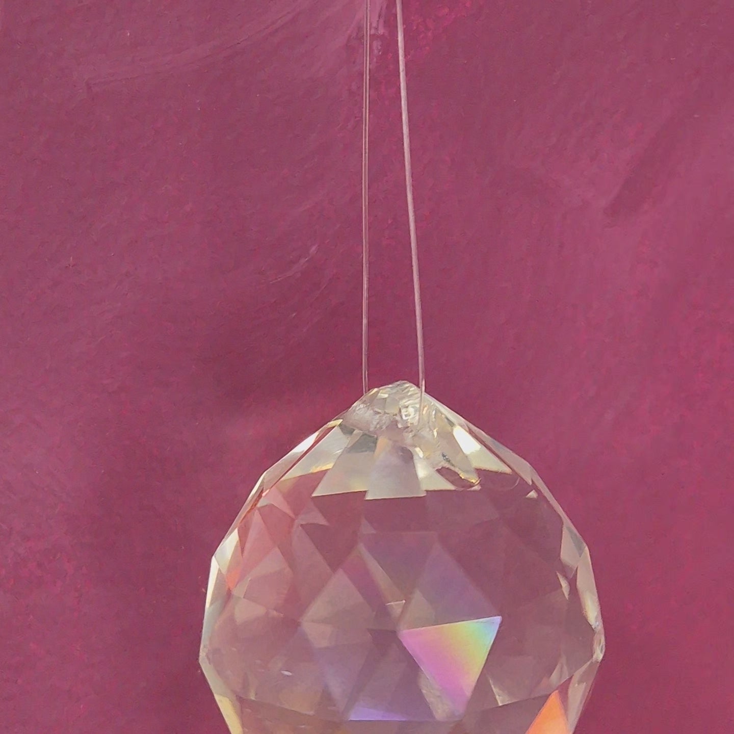 Faceted crystal feng shui is hanging and spinning around in a magenta bacground