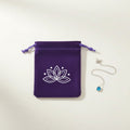 Purple velvet pouch with white lotus design beside silver necklace with blue gemstone