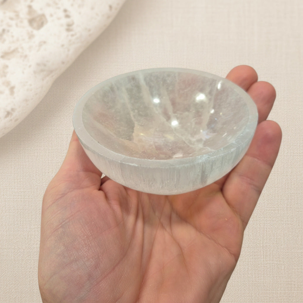 Clear selenite stone bowl held in a hand against a neutral background