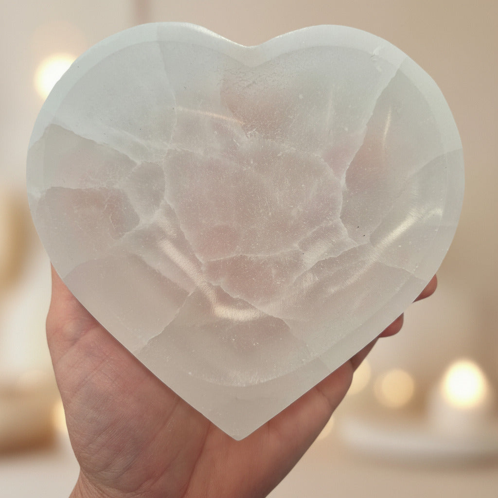 Heart-shaped selenite held in a hand with a blurred background