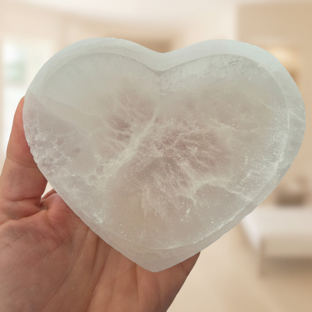 Heart-shaped selenite stone held in a hand with a blurred background