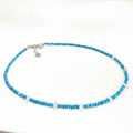 A beaded necklace featuring bright turquoise blue beads and a few translucent white beads, with a silver-tone clasp and heart charm, displayed on a white surface.