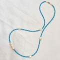 A beaded necklace featuring bright turquoise blue beads and irregular white pearl-like accents, laid out on a white fabric background.