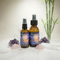 Two bottles of 'smokeless smudge spray' with colorful labels on a white surface with crystals and bamboo.