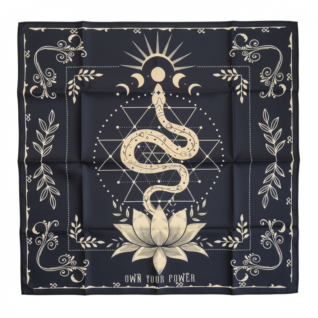 A square black bandana or scarf laid flat on a white surface featuring a cream-colored mystical design with a snake, sun, moon, lotus flower, geometric symbols, and decorative borders. The text 'OWN YOUR POWER' is printed on the right side.